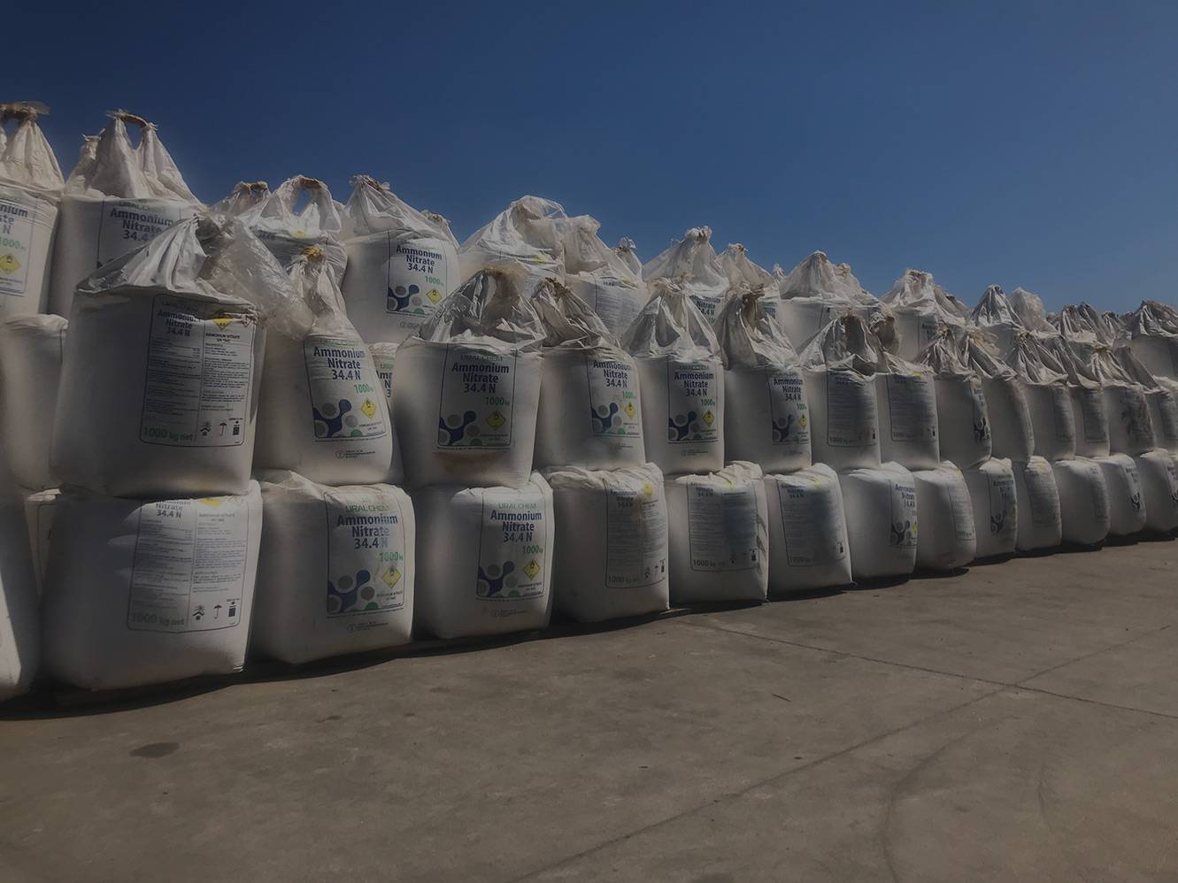 A long row of white bulk bags stored in a yard.