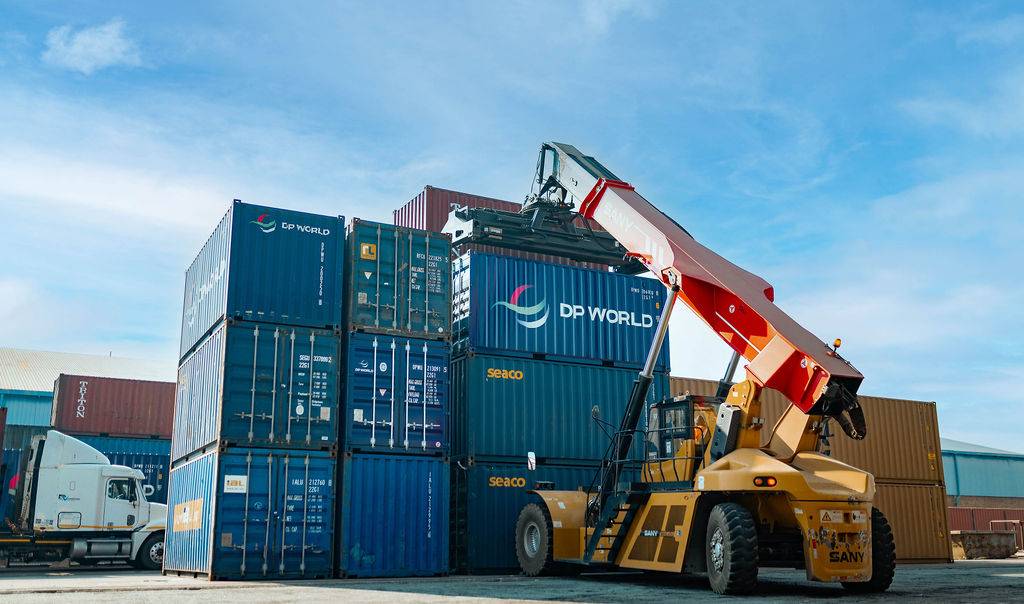 A reach stacker handling DP World containers in a stacked container yard.